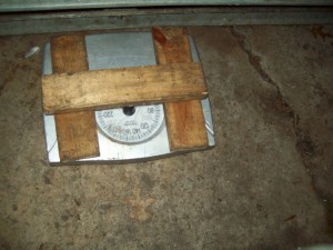 A view of an analog scale under a garage door in order to weight it.