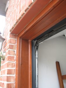 A side view of an oak-looking garage door with top and side weatherstripping seals. 