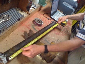 An image of a person measuring a torsion spring using a tape measure.
