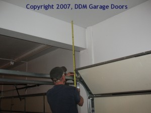 A professional using a tape measure to determine the distance between the ceiling and the top of the garage door.