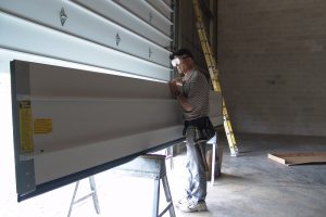 Dan Musick balancing a white garage door section on a sawhorse.