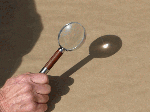 A man holding magnifying glass that is reflecting a single light onto the surface symbolizing a businesses kingdom purpose.