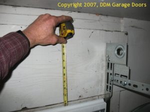 A person using a tape measure is measuring from a mark to the top of the garage door.