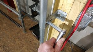 A person removing the nuts and bolts off of a bracket that is secured to the garage door track.