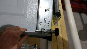 A person pulling down on the door until the bottom roller is shown clearing the bottom of the flag bracket. 