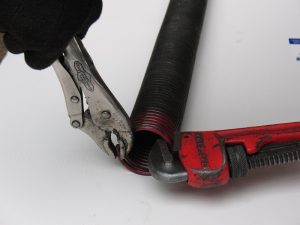 A person using a vise-grip and pipe wrench to bend the end of the spring wire.