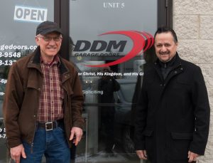 A picture of Dan Musick standing  with Ray Bansal outside of DDM Garage Doors office.