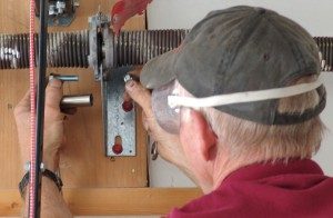 A repair professional loosening and removing the two bolts that secure the center stationary torsion cones on a garage door spring.
