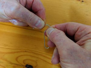 Hands are bending a paper clip over a wooden surface.
