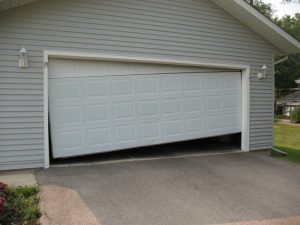 A white crooked garage door with the right side of the door lifted off the ground.