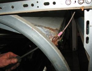 A rusted garage door cable being removed with a screwdriver.