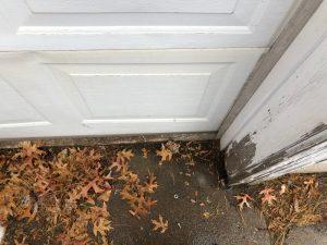 A view of a garage door with leaves by the bottom seal of the door.