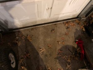 A picture showing a white garage door with some leaves around the bottom seal.