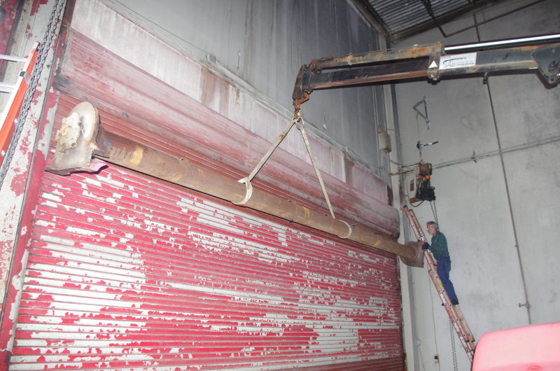 A view of the barrel of a steel rolling door being supported by a crane in order to replace steel rolling door springs.