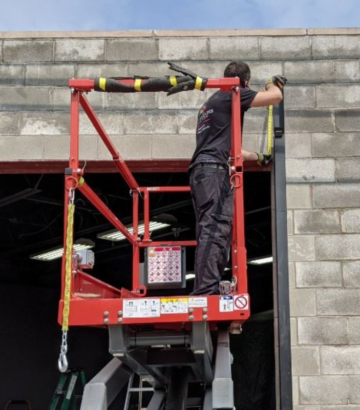 A garage door installer is measuring both sides from the level steel header.