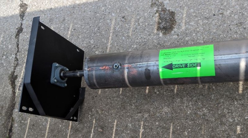 A steel rolling door barrel with a bright green sticker pointing to the drive side of the barrel.