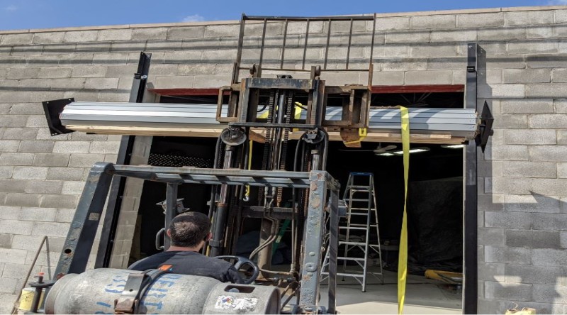 A steel rolling door curtain supported by two by fours being raised by a forklift.