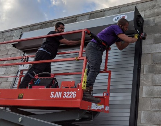 Two installers standing on a scissor lift skyjack securing a curtain door hood.