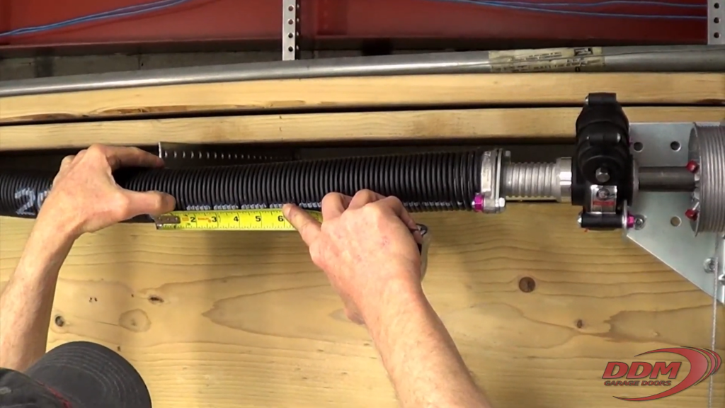 Measuring the width of the coils on the torsion spring. Set the tape measure in one end, count the number of coils starting with where the tape measure is set, then see the distance between the first and last coil counted.